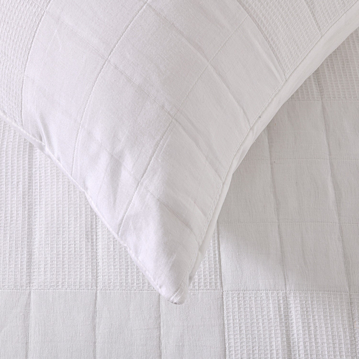 White quilted coverlet close-up showing textured fabric and diamond stitching detail.