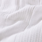 White quilted coverlet close-up showing textured fabric and diamond stitching detail.