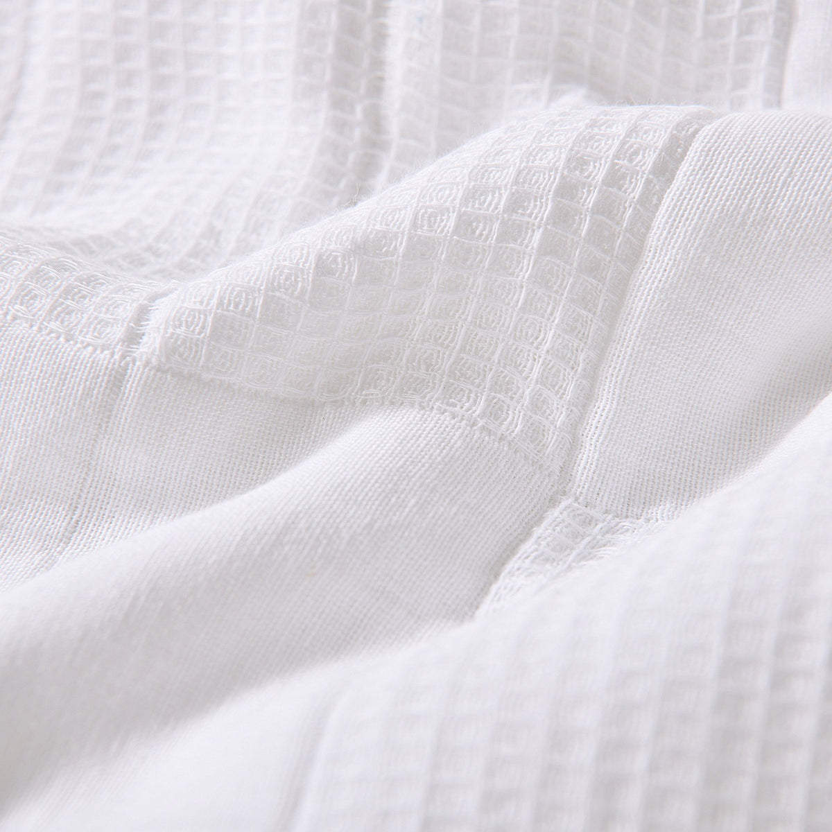White quilted coverlet close-up showing textured fabric and diamond stitching detail.