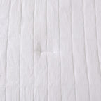 White quilted coverlet close-up showing textured fabric and diamond stitching detail.
