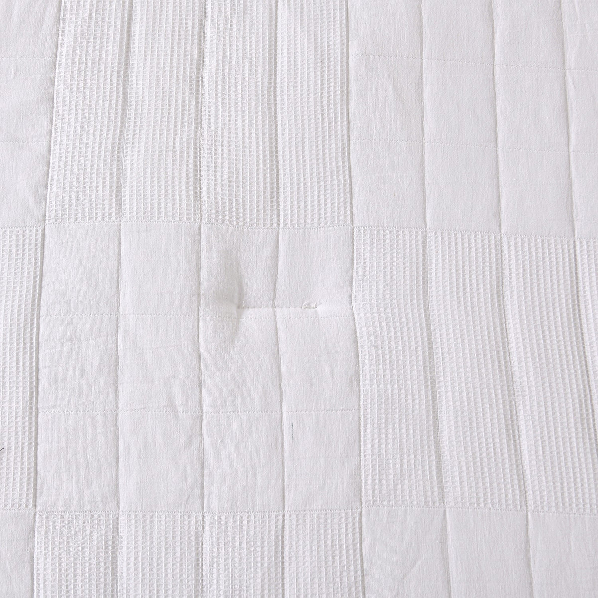 White quilted coverlet close-up showing textured fabric and diamond stitching detail.