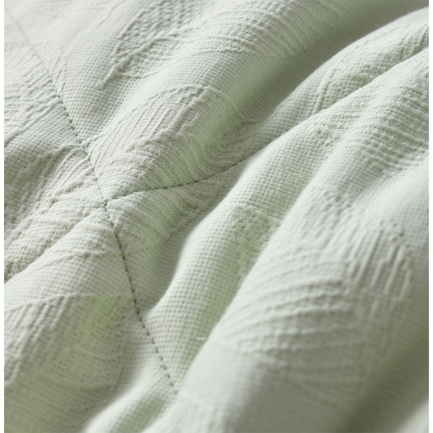 Light green quilted coverlet close-up showing soft textured fabric and stitched detail.