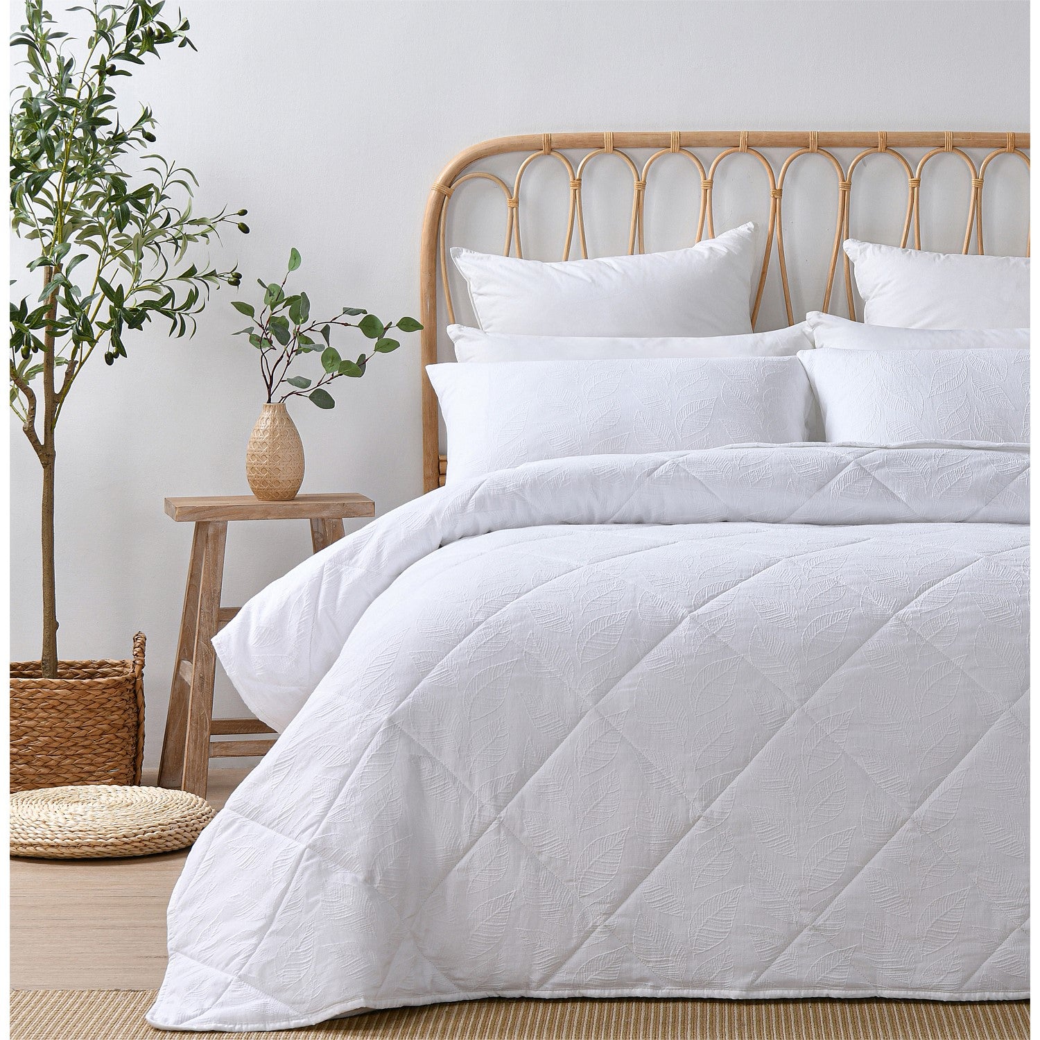 White quilted coverlet set styled on a bed in a bright neutral bedroom.