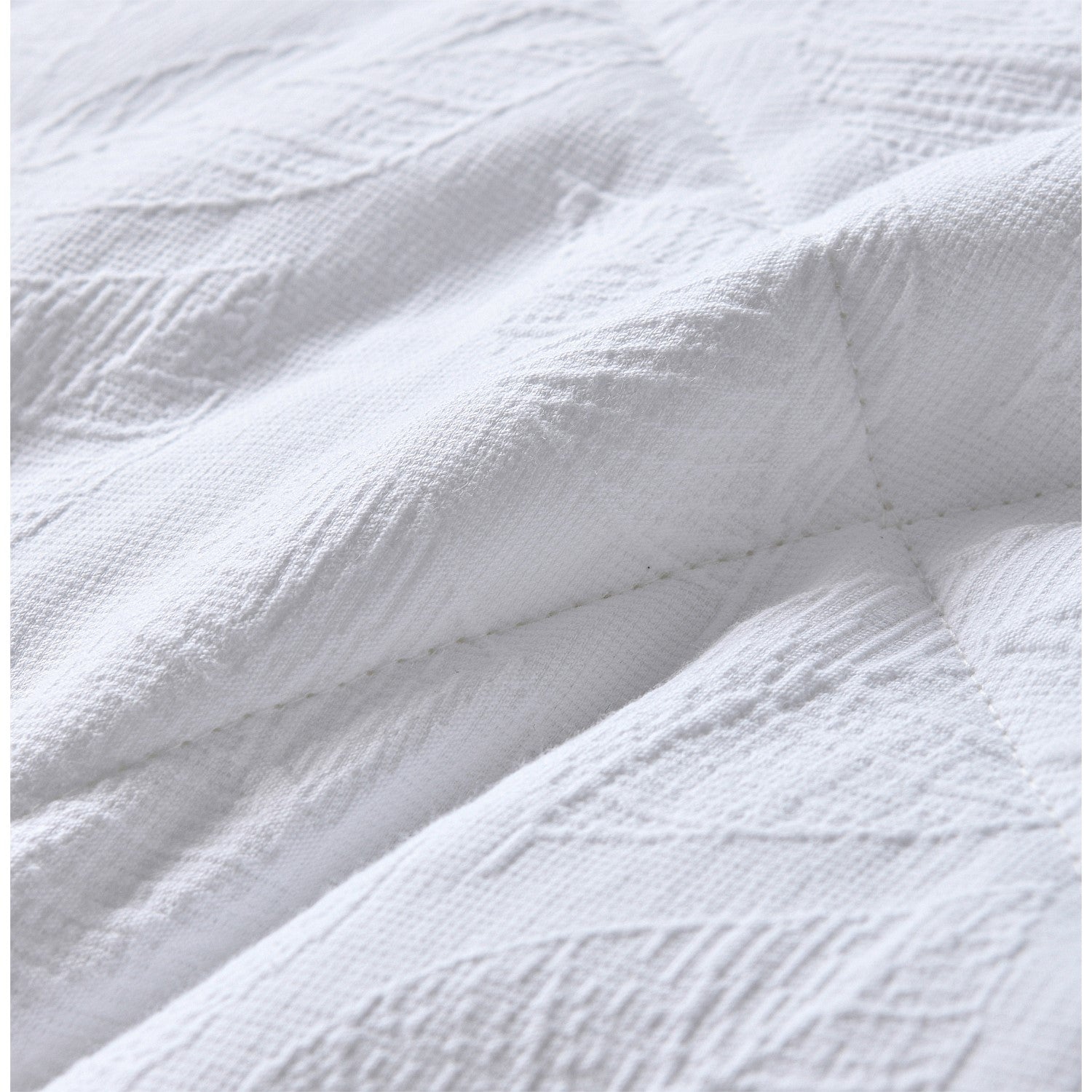 White quilted coverlet close-up showing soft textured fabric and stitched detail.