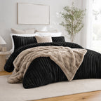 Black ribbed comforter set styled on a bed with matching pillows and a faux fur throw in a neutral bedroom.