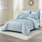 Angled view of a cornflower blue comforter set with gathered panels, textured ruching, pleated detailing, and matching decorative cushions, styled in a light and airy bedroom.