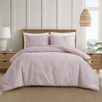 Blush pink patterned comforter set styled on a bed with matching pillowcases in a bright neutral bedroom.