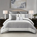 A styled bed dressed in a slate blue comforter set with beige and white decorative pillows, set against a textured gray wall with a side table and vase.