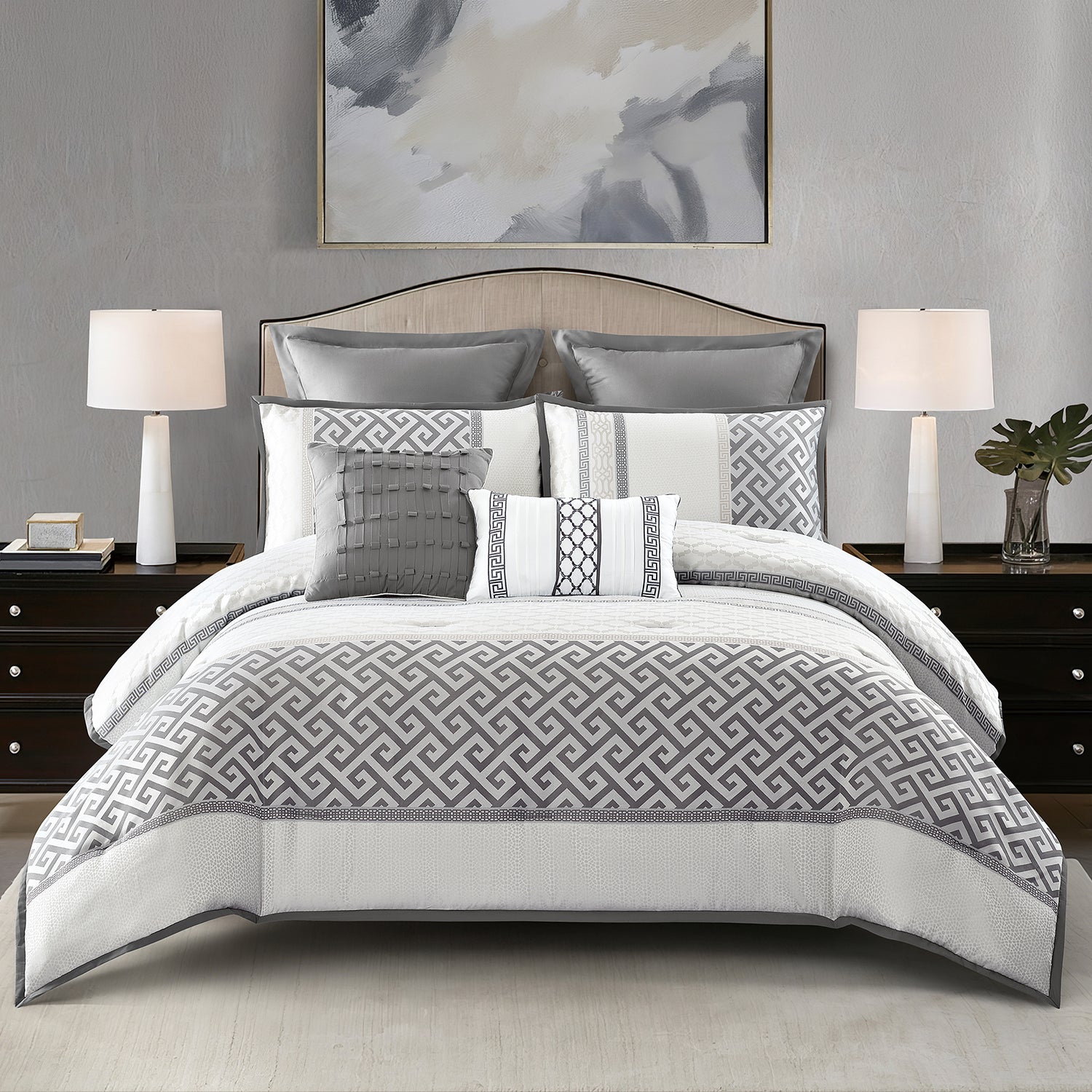 A styled bed dressed in a slate blue comforter set with beige and white decorative pillows, set against a textured gray wall with a side table and vase.