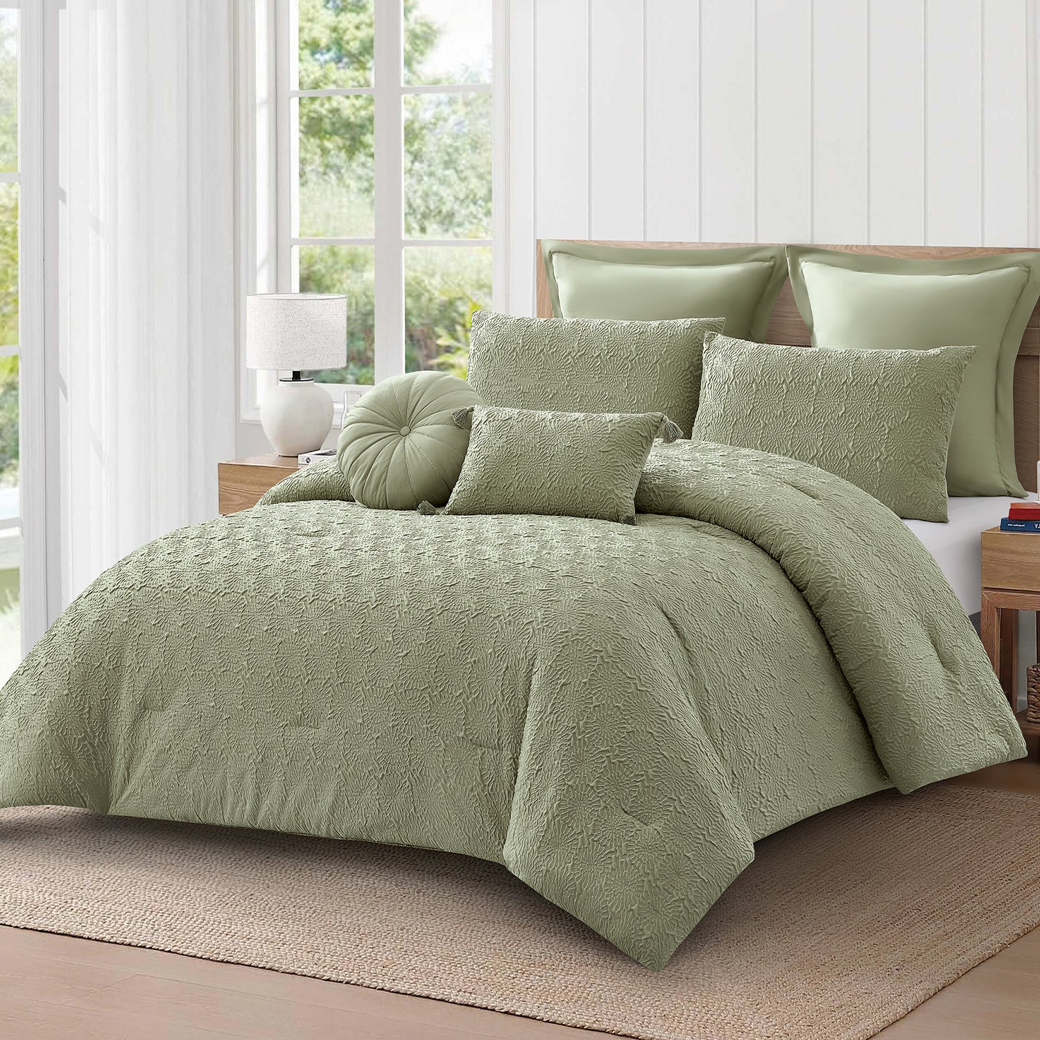 Angled view of the sage green textured 7-piece comforter set with coordinating pillows and cushions on a wooden bed in a light-filled bedroom.