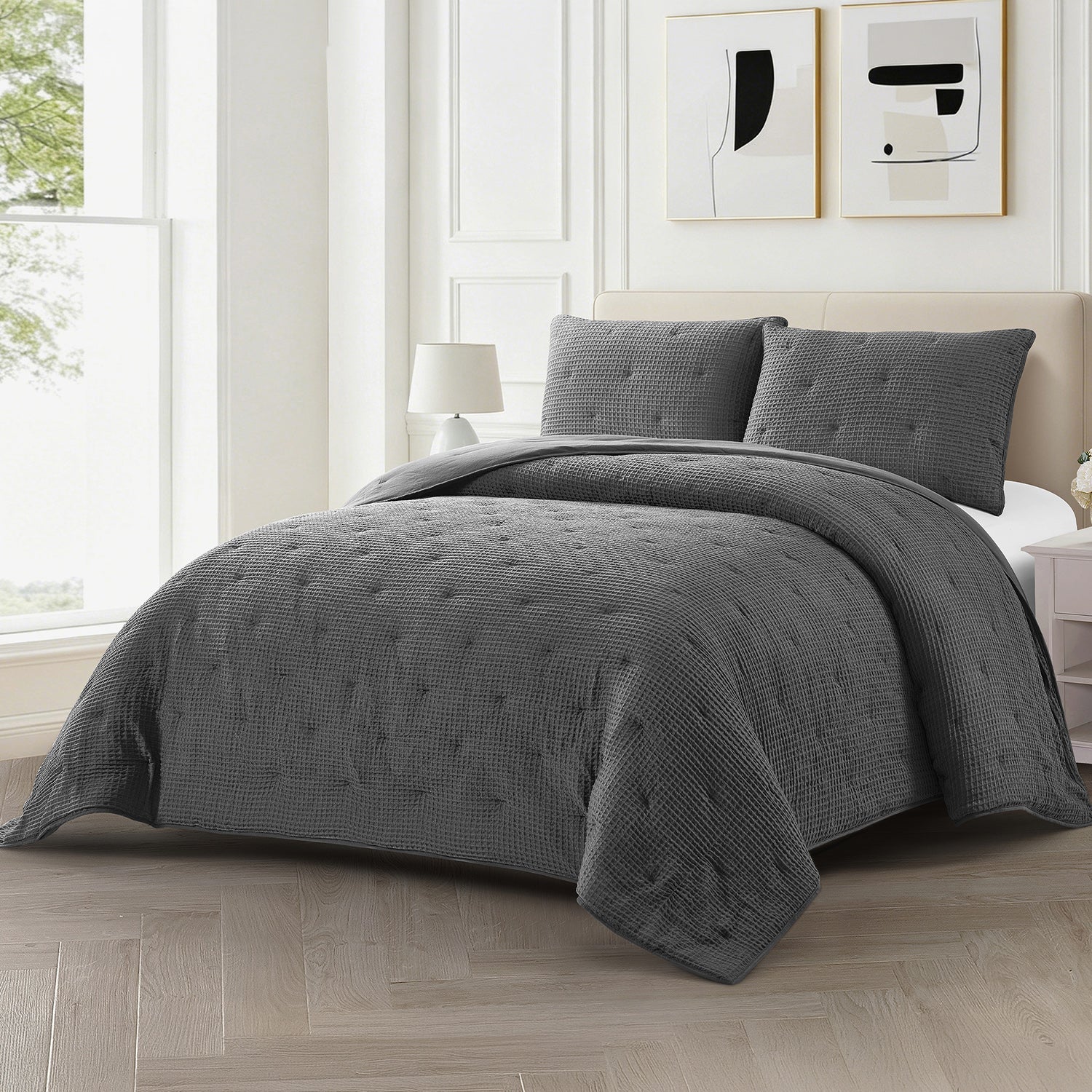 A dark gray textured quilted bedding set with matching pillow shams on a bed in a bright, modern bedroom.