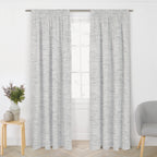 Pair of grey blockout ready-made curtains with a subtle textured weave hanging from a silver curtain rod in a bright living room.