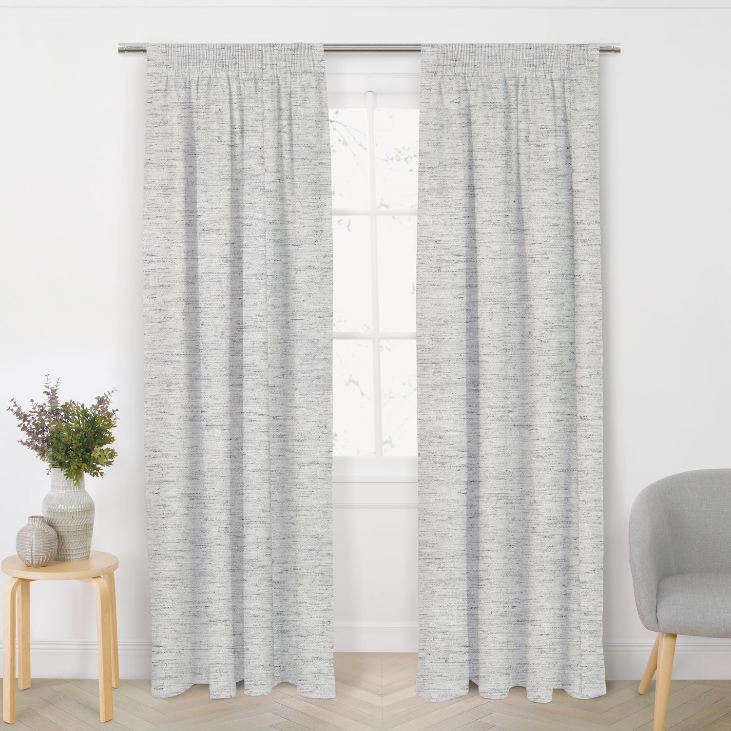 Pair of grey blockout ready-made curtains with a subtle textured weave hanging from a silver curtain rod in a bright living room.