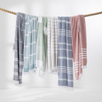 Striped beach towels in assorted soft colours draped over a natural rope.