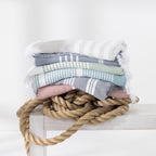 Stack of striped beach towels in soft coastal colours styled with natural rope.