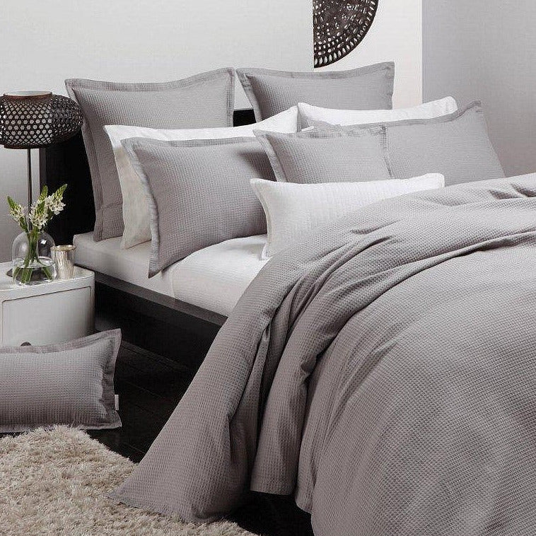 Gray bedding set on a bed with a nightstand in the background
