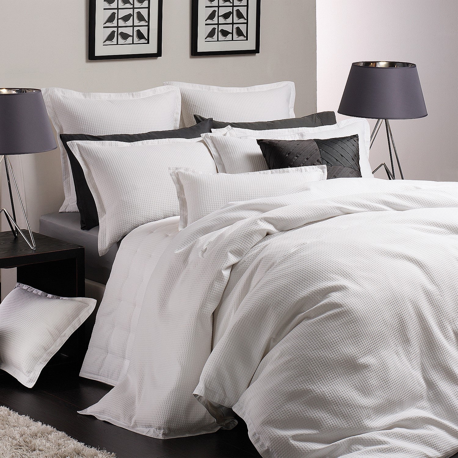 Neatly made bed with white bedding and black pillows in a bedroom setting.