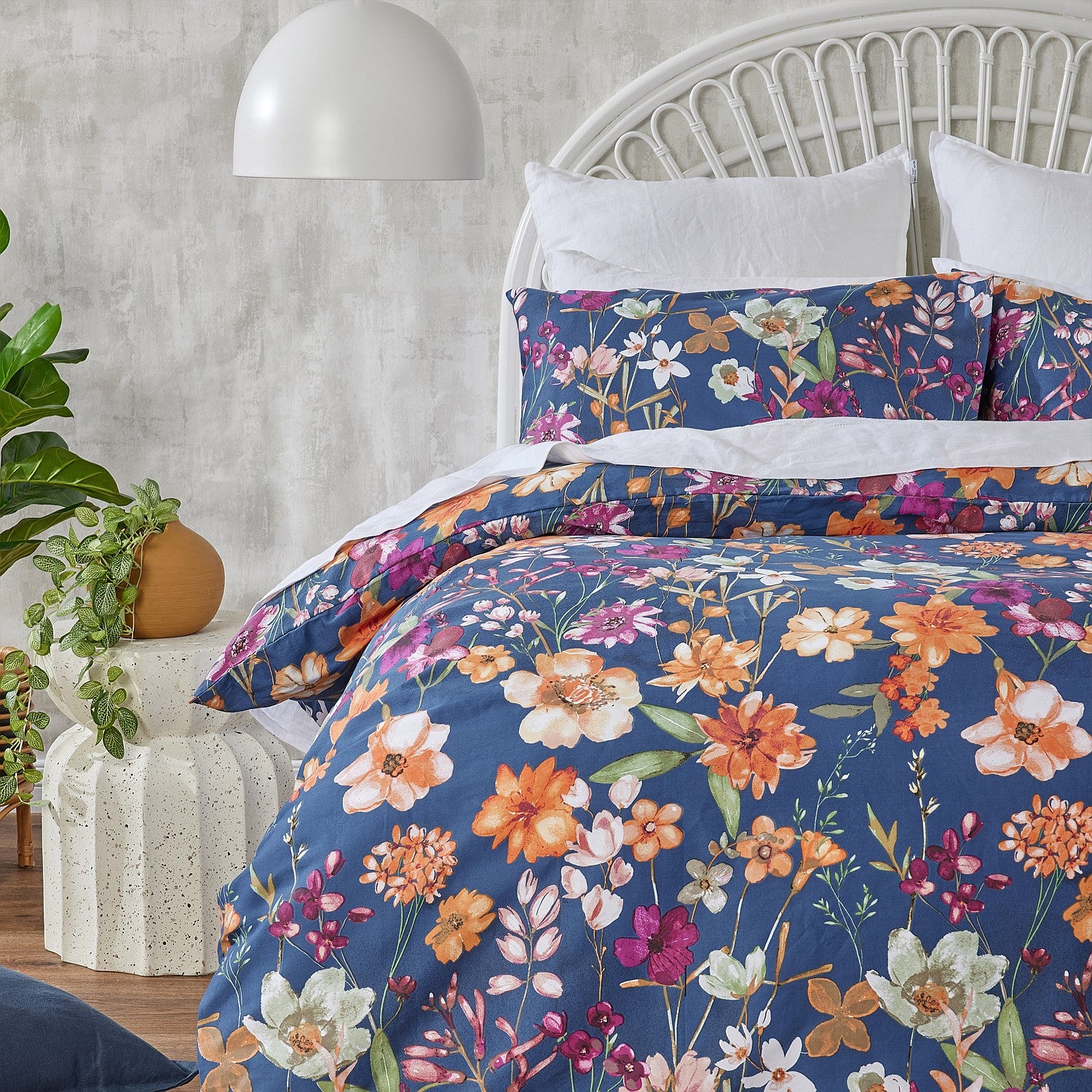 Floral bedding set on a bed with a white headboard and decorative plants.