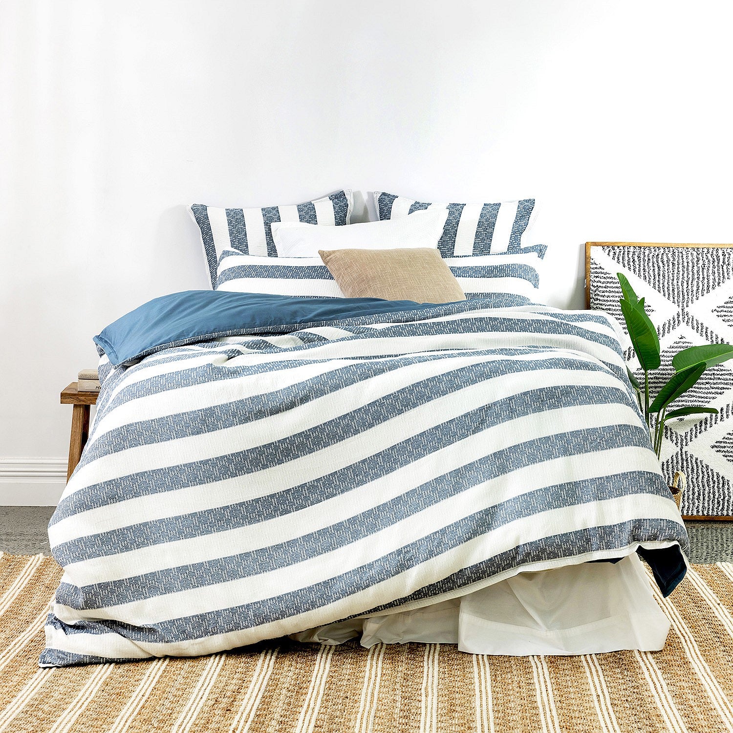 Striped bedding set on a bed with pillows and a plant in a bedroom.