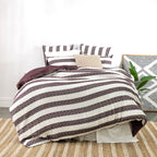 Striped bedspread on a bed with pillows and a plant in a room.
