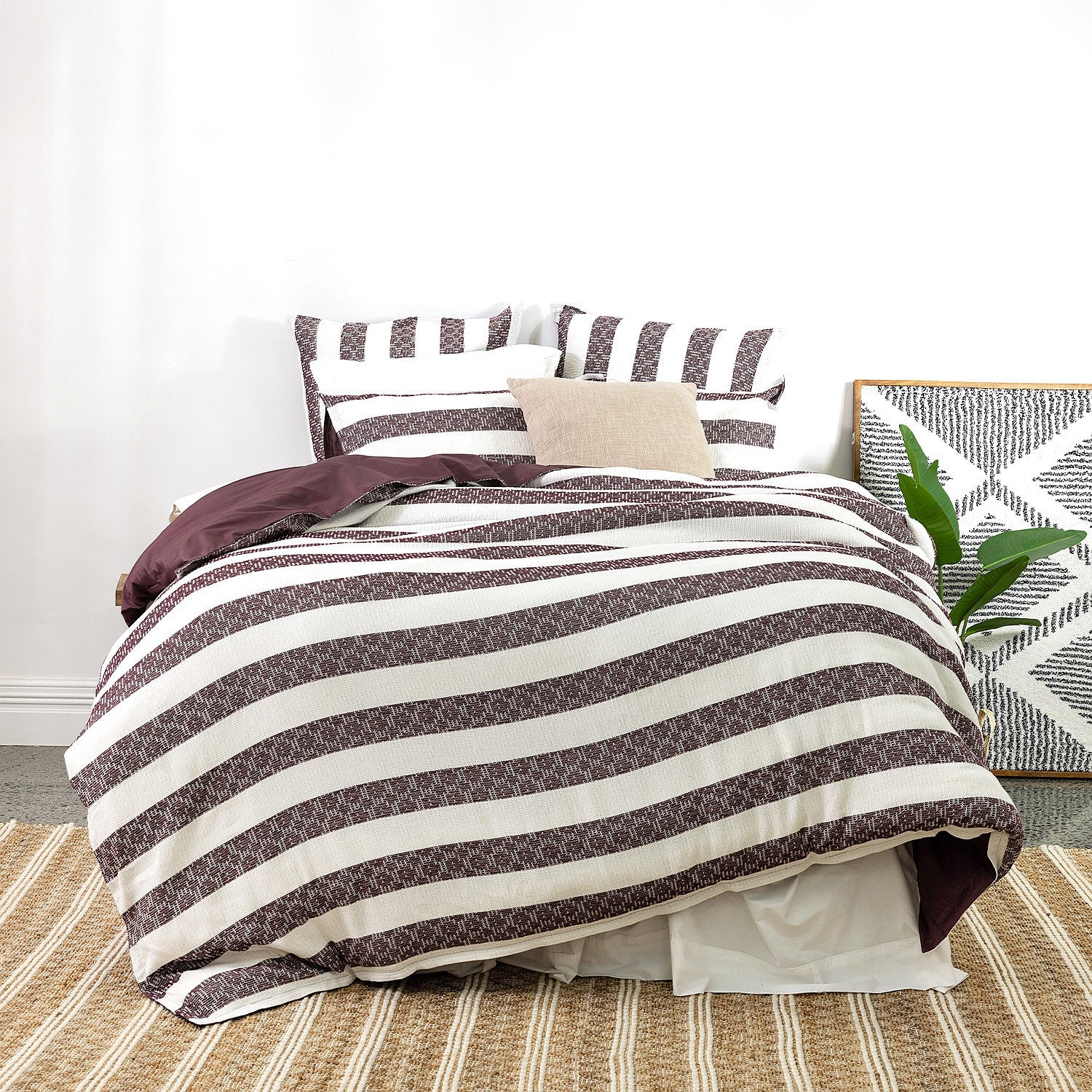 Striped bedspread on a bed with pillows and a plant in a room.