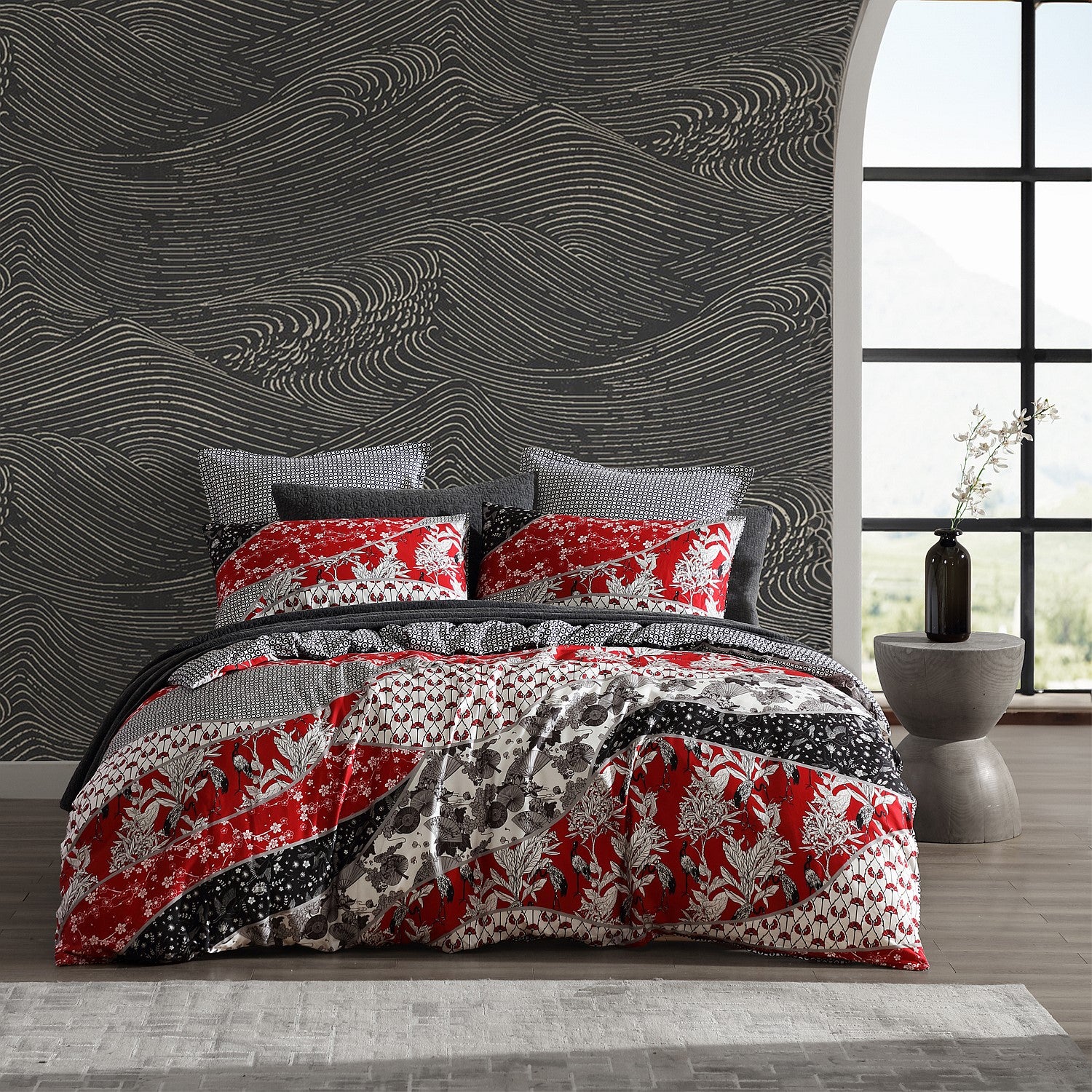 Bed with red and gray patterned bedding in a room with a textured wall and large window.