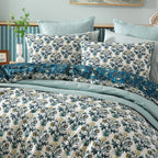 Floral patterned bedding set on a bed with light blue walls and a plant in the background.