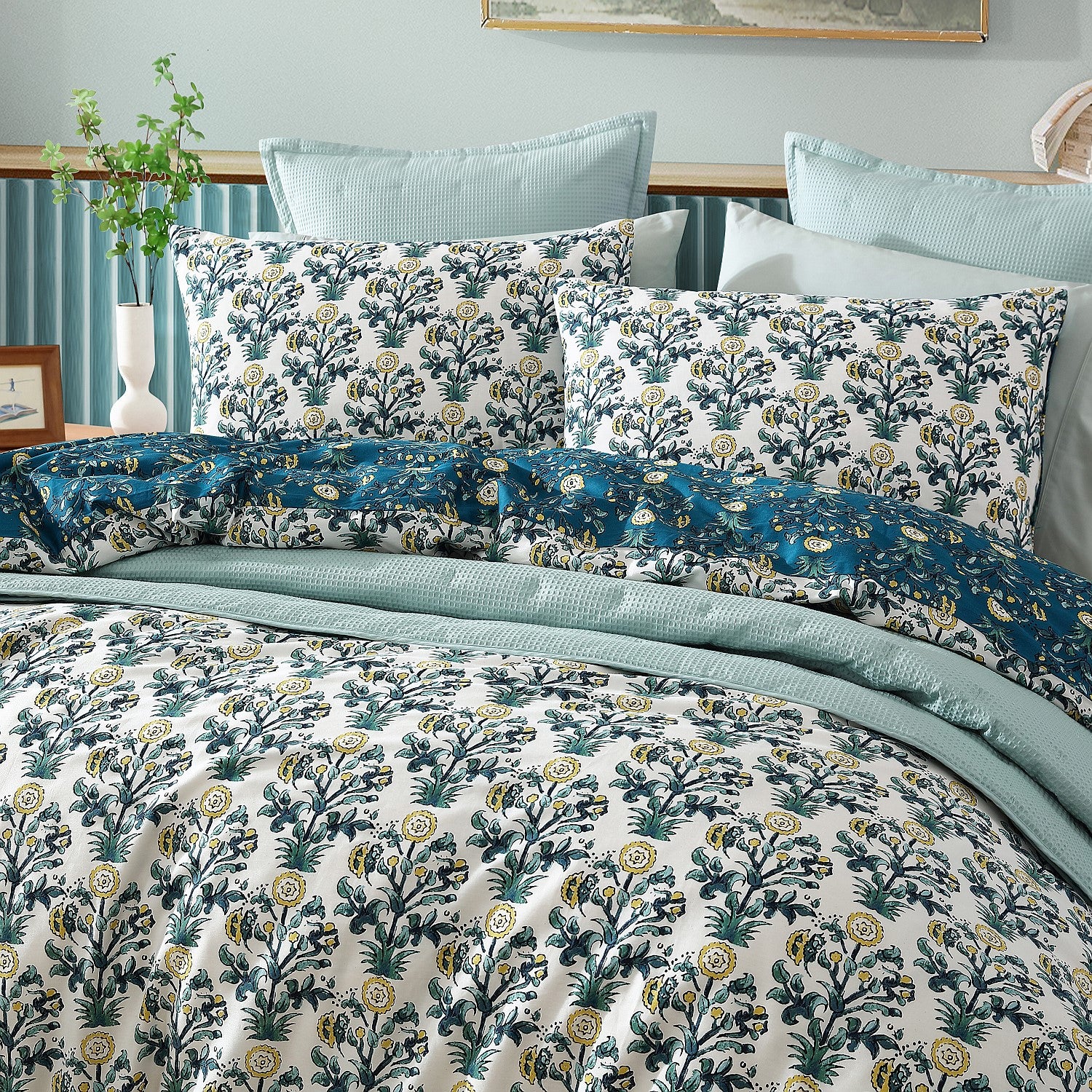 Floral patterned bedding set on a bed with light blue walls and a plant in the background.