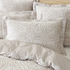 Patterned beige and white bedding set with pillows on a bed.