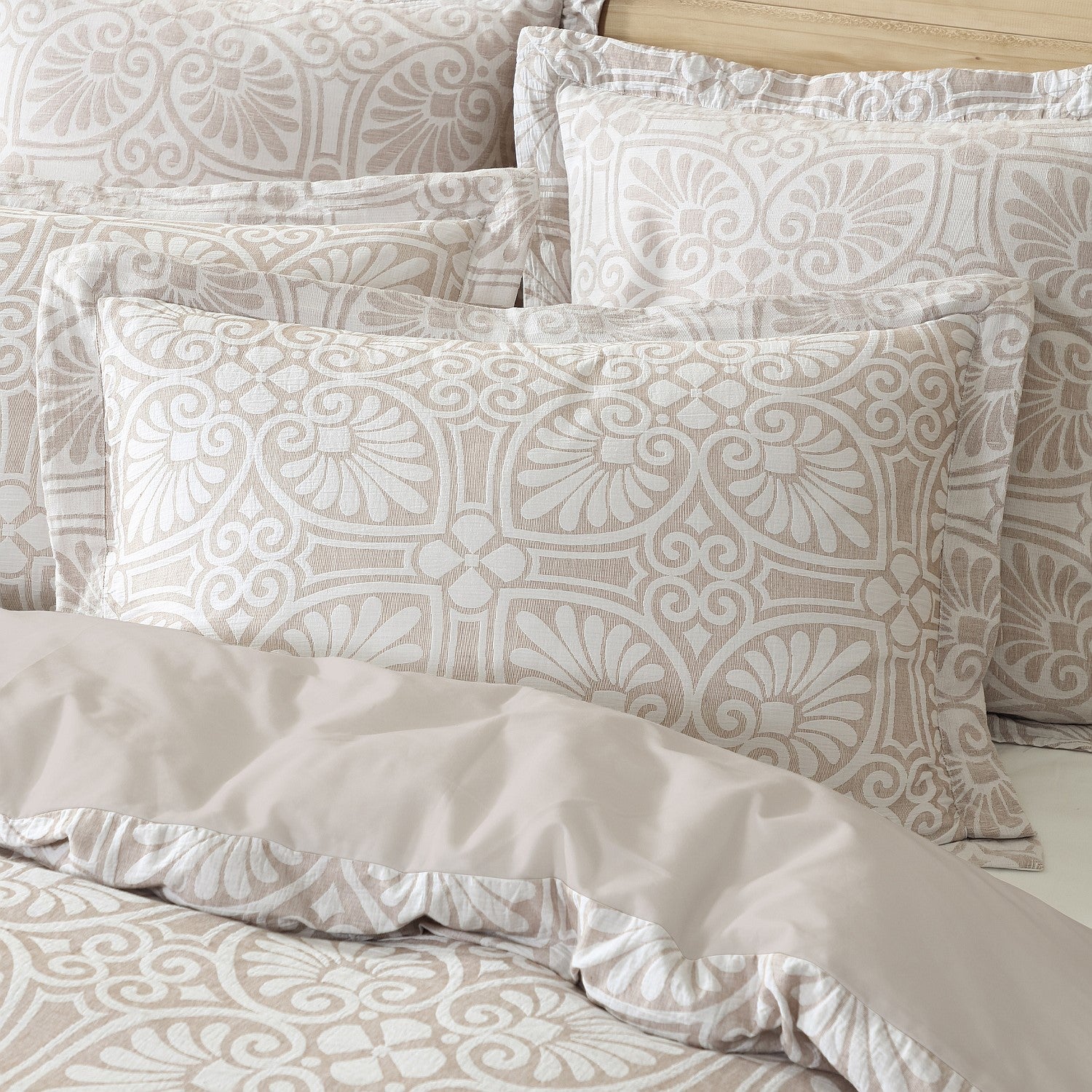 Patterned beige and white bedding set with pillows on a bed.