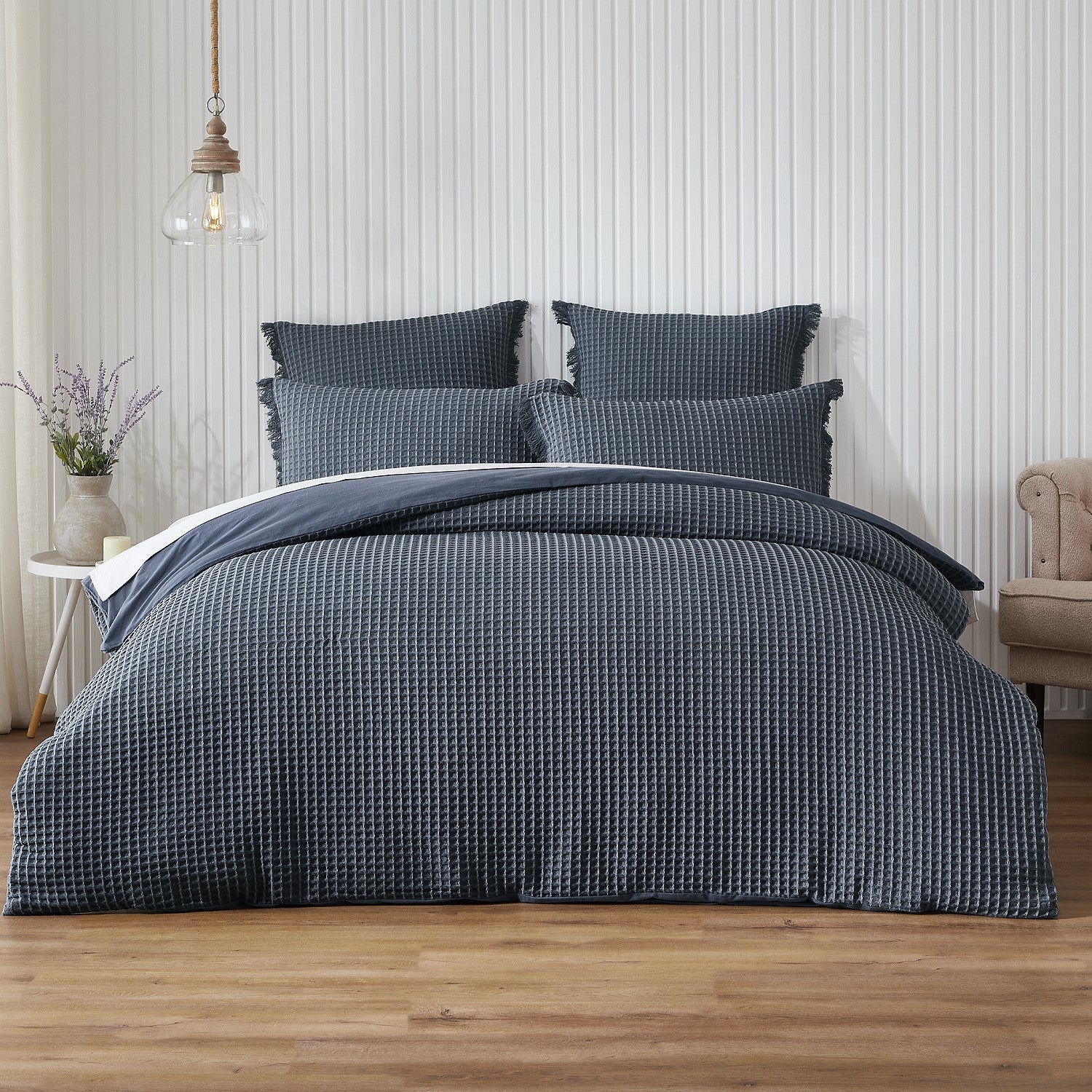 Blue textured bedding set on a bed in a bedroom with wooden flooring and a striped wall.