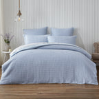 Blue textured bedding set on a bed in a bedroom with wooden flooring and a neutral wall.