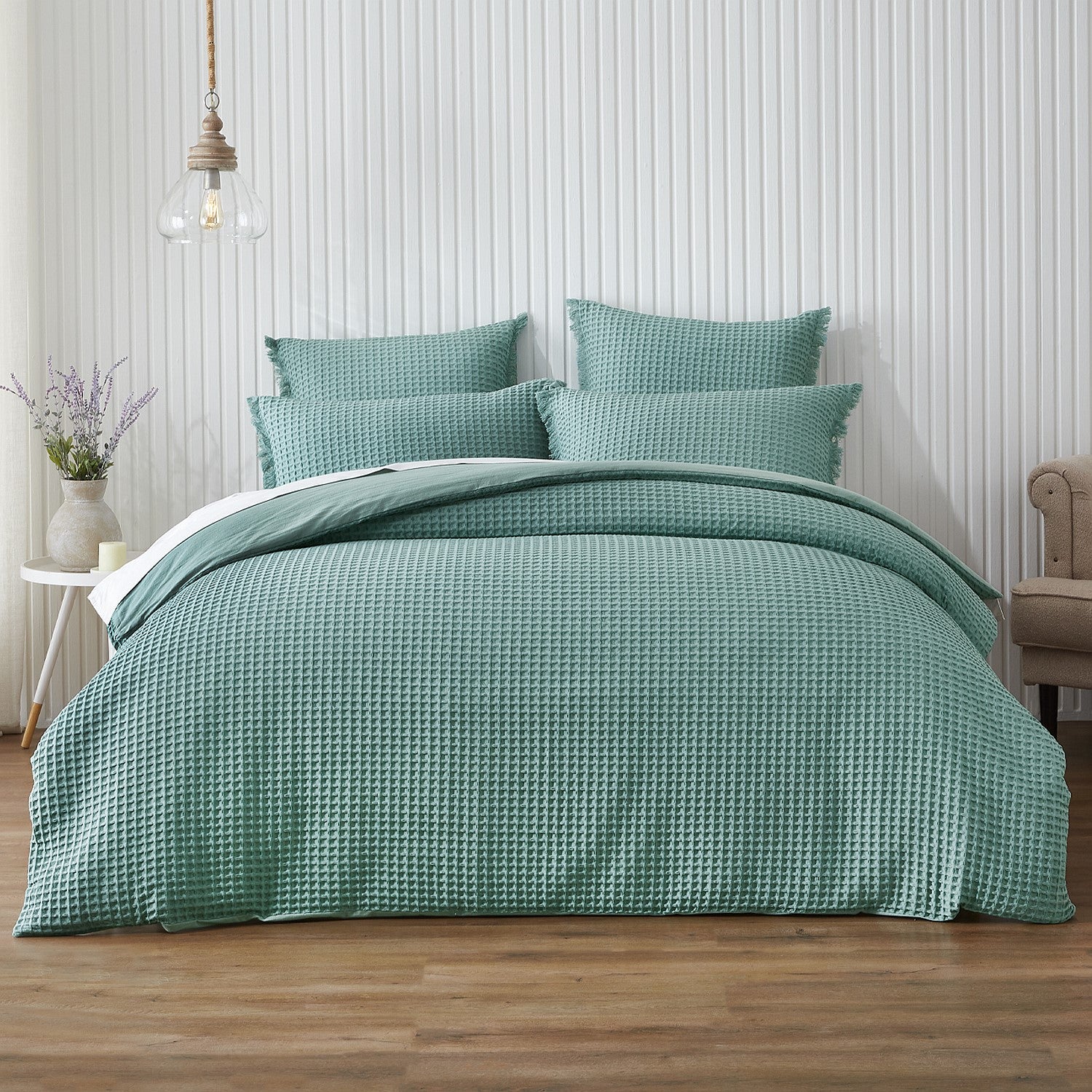 Teal bedding set on a bed in a bedroom with wooden flooring and a white wall.