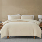 Beige quilted comforter set on a bed with pillows against a beige wall.