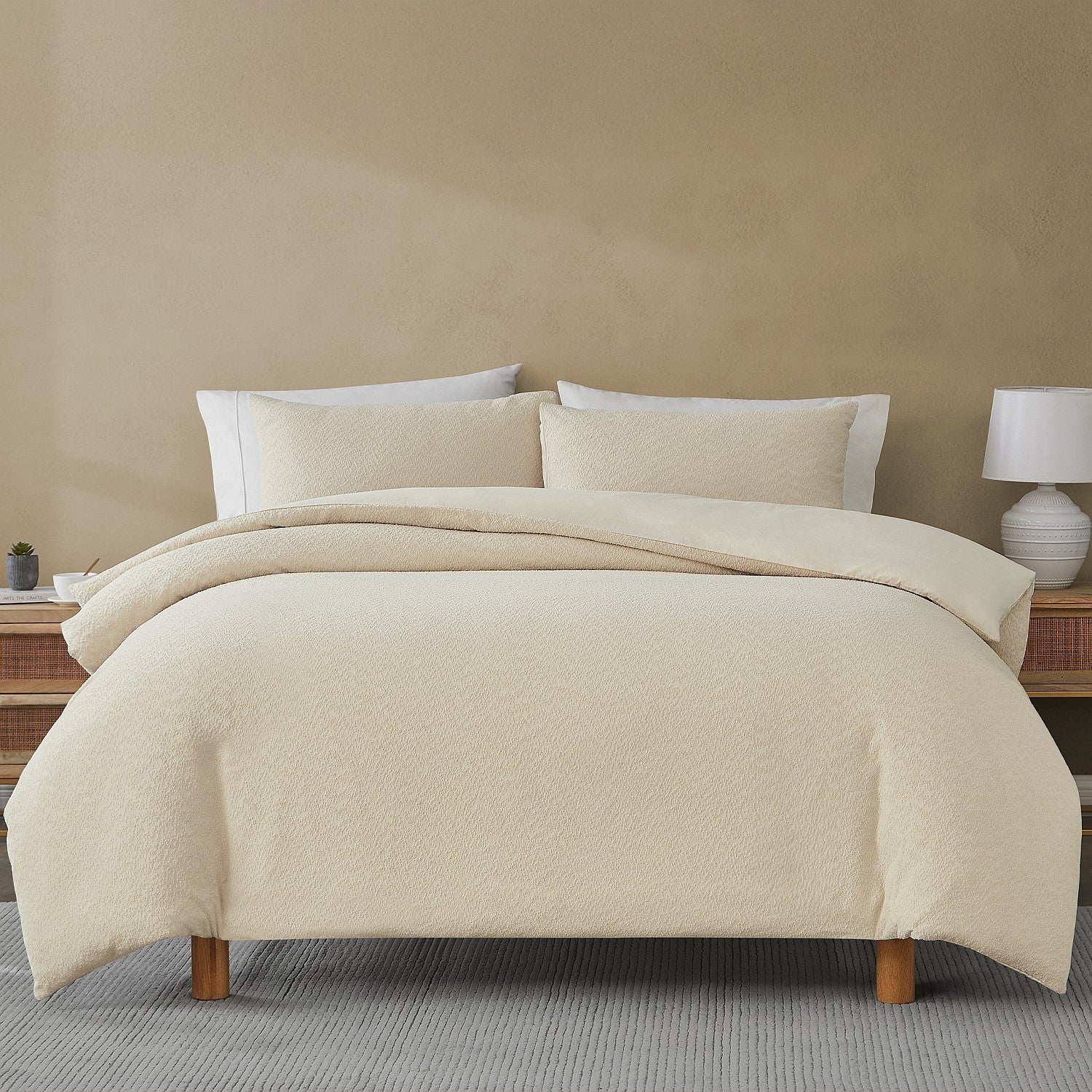 Beige quilted comforter set on a bed with pillows against a beige wall.