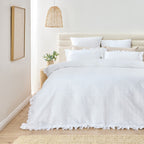 White textured duvet cover on a bed in a bright bedroom with a lamp and plant.