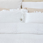Close-up of white textured bedding with ruffled edges on a bed.