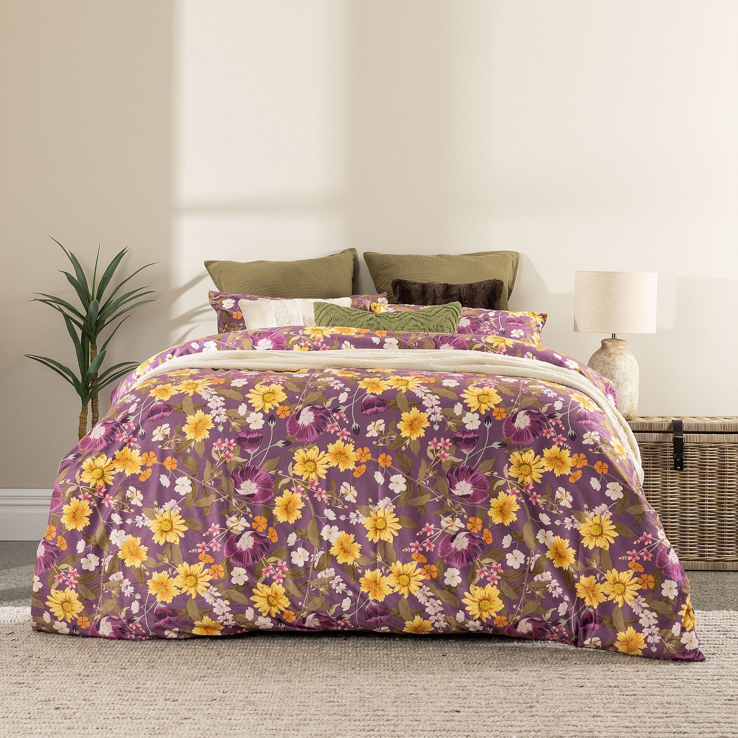 Floral patterned comforter on a bed in a room with a plant and lamp.