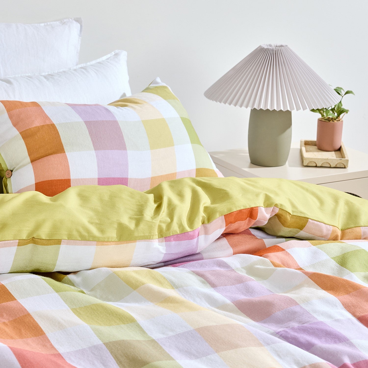 Colorful checkered bedspread on a bed with a lamp and plant in the background.