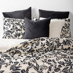 Floral patterned bedding with black and white pillows on a bed.
