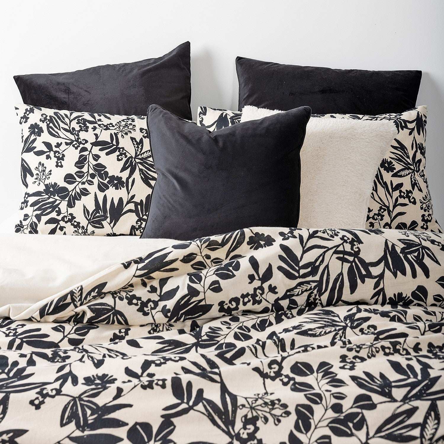 Floral patterned bedding with black and white pillows on a bed.