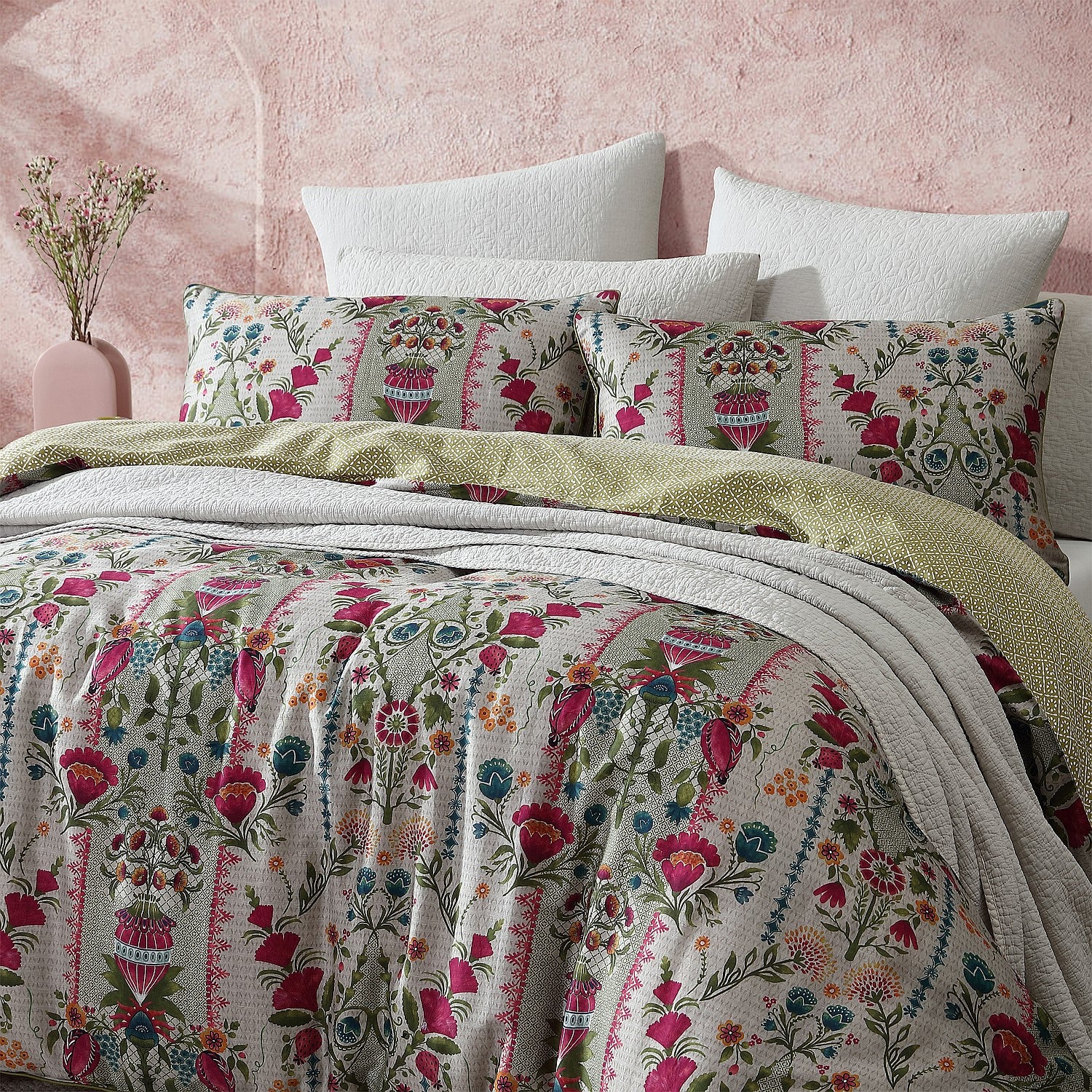 Floral bedding set on a bed with a pink textured wall in the background