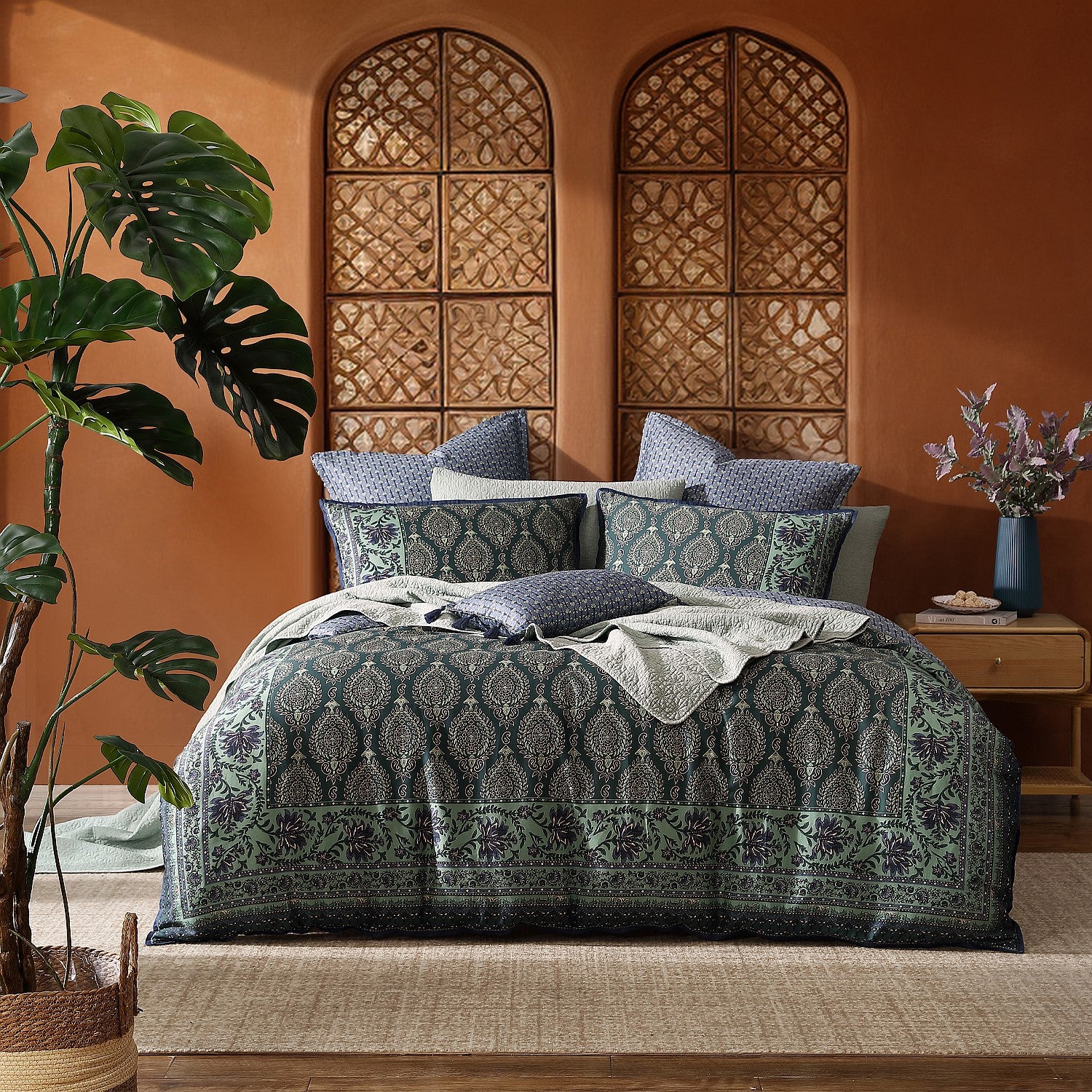 Decorative bedding set on a bed with a patterned headboard and plants in a room.