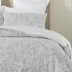 Gray patterned bedding set on a bed with white pillows against a neutral wall.