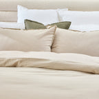 Neatly made bed with beige and white bedding and pillows.