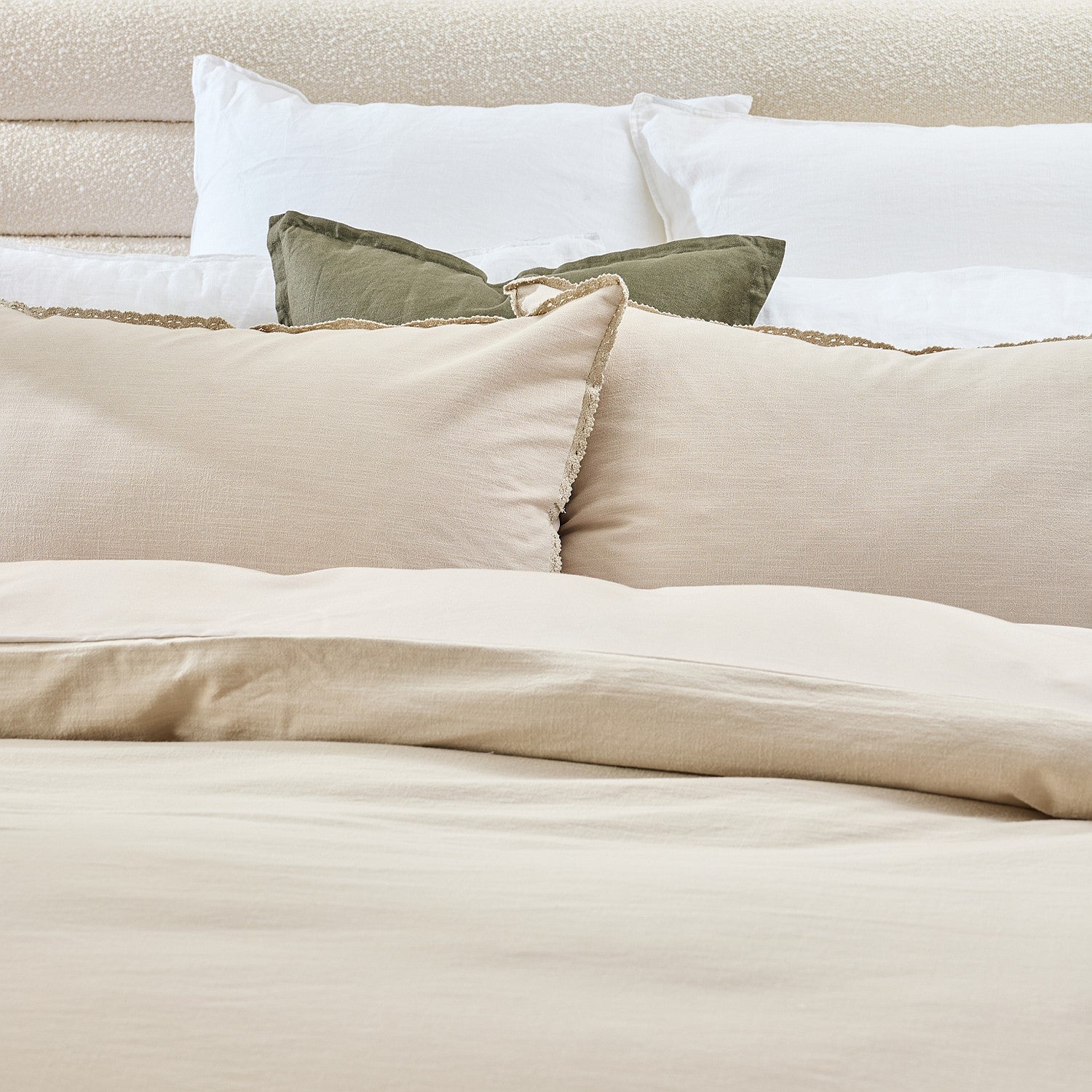 Neatly made bed with beige and white bedding and pillows.