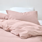 Pink bedding set with pillows on a bed against a white background