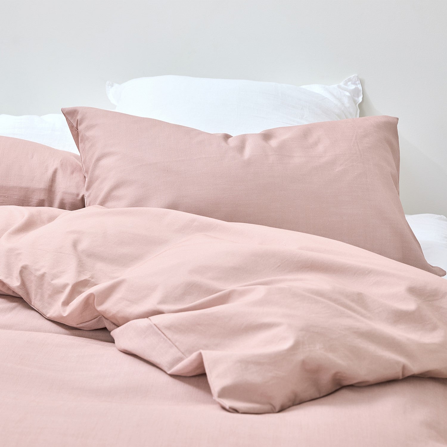 Pink bedding set with pillows on a bed against a white background