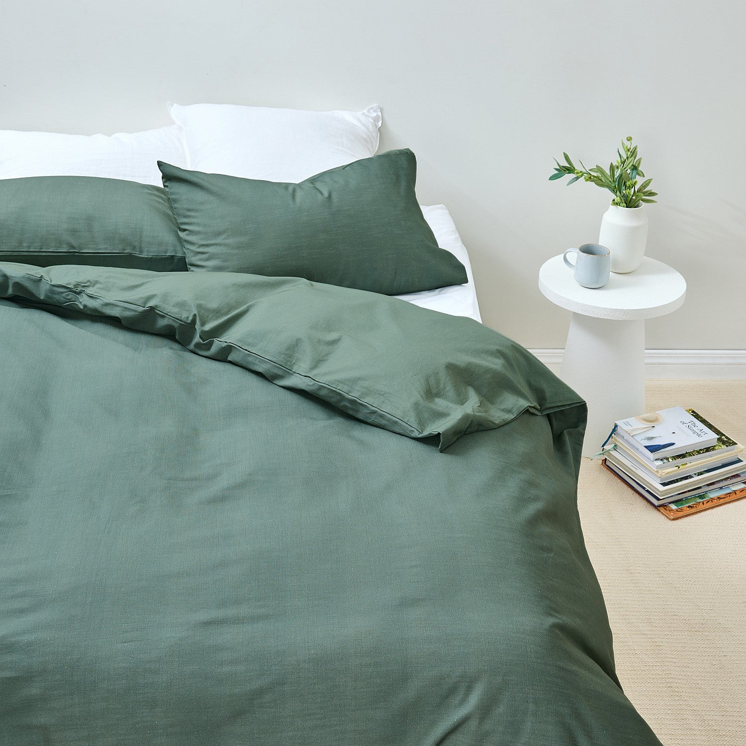 Green bedding set on a bed with a side table and books in the background.