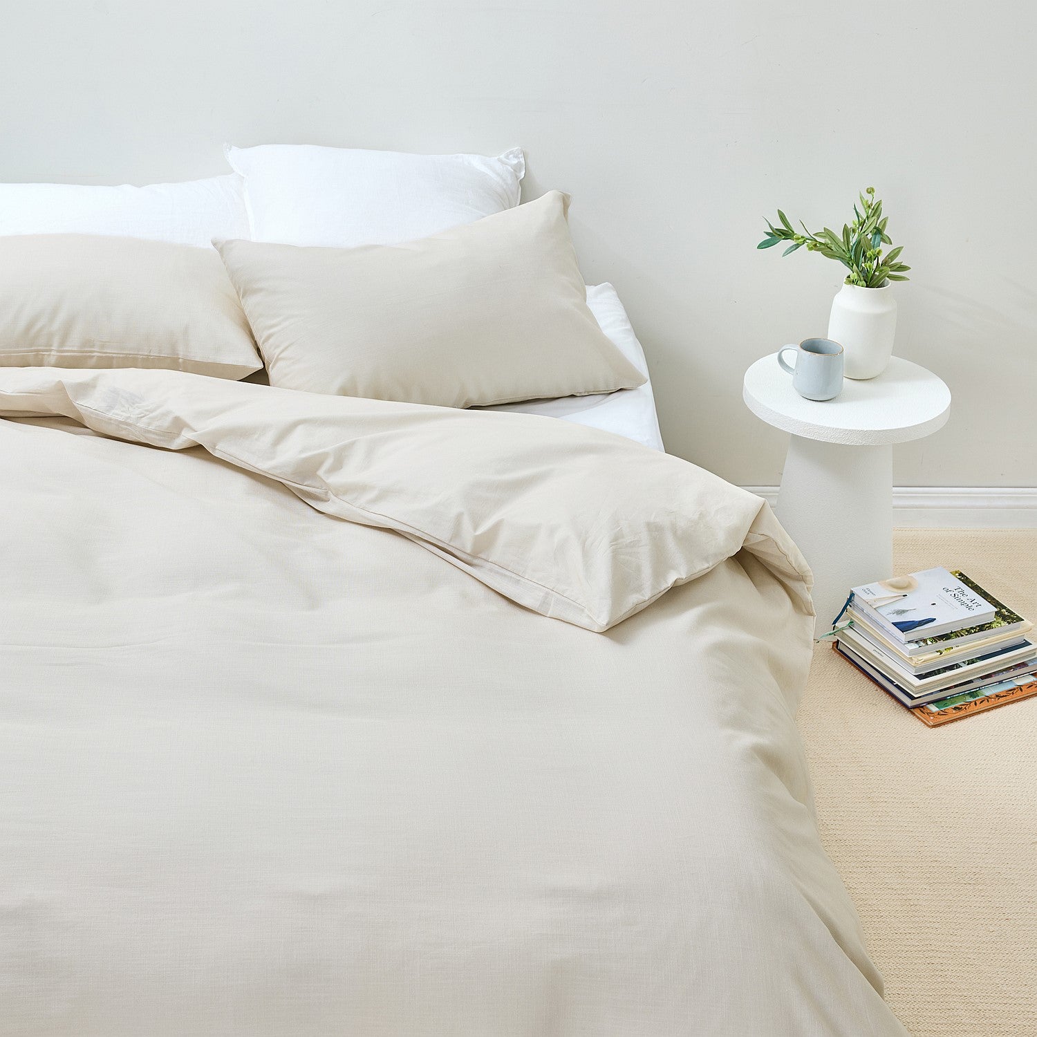 Beige bedding set on a bed with a side table and books in the background